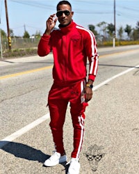 a man in a red tracksuit is standing on the side of the road